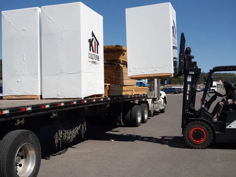 Forklift loading packaged home kits onto a flatbed truck for delivery to the build site